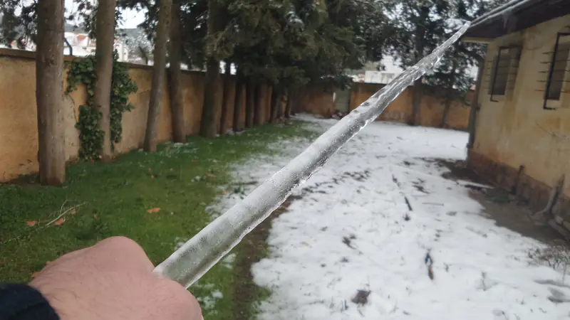 Ein langer Eiszapfen wird in einem verschneiten Garten neben einem Haus gehalten