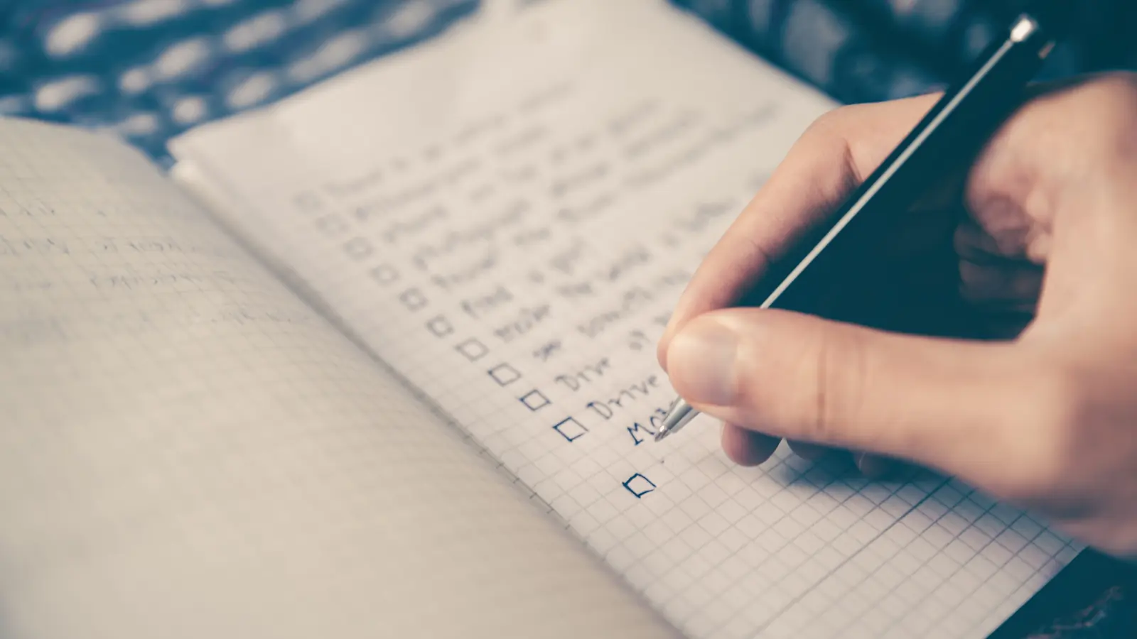 Eine Hand schreibt eine Checkliste in ein kariertes Notizbuch